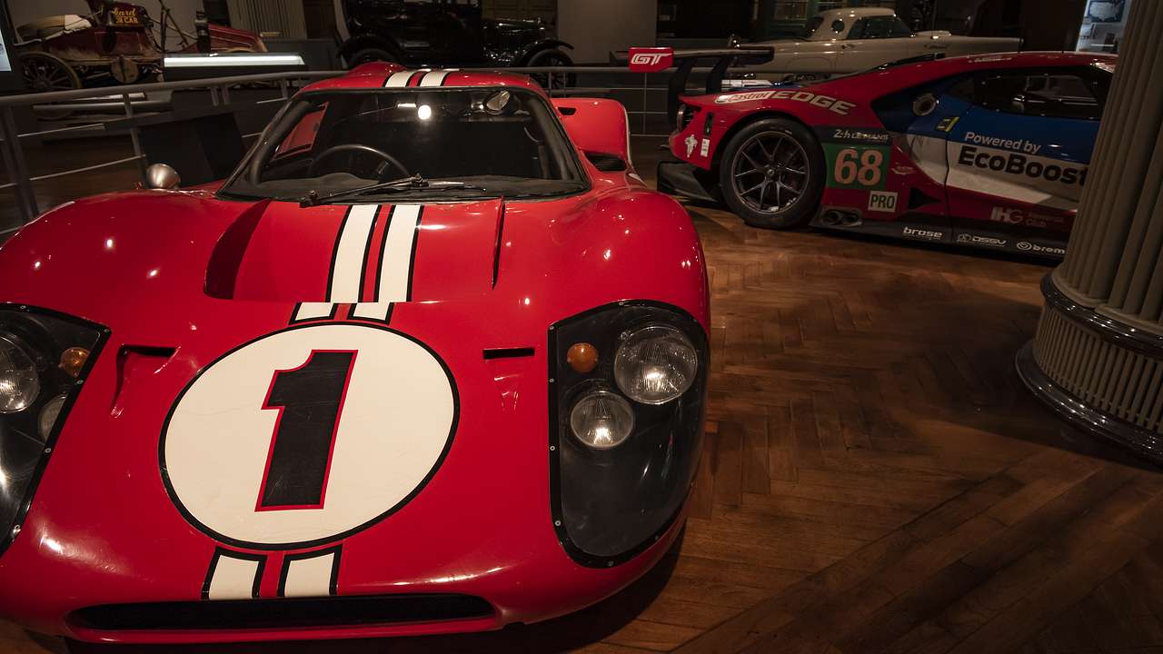 A red sports car with number one on its hood among other cars in a museum
