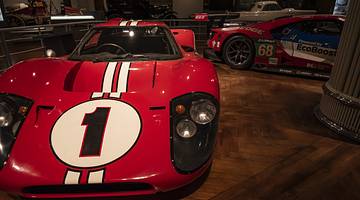 A red sports car with number one on its hood among other cars in a museum