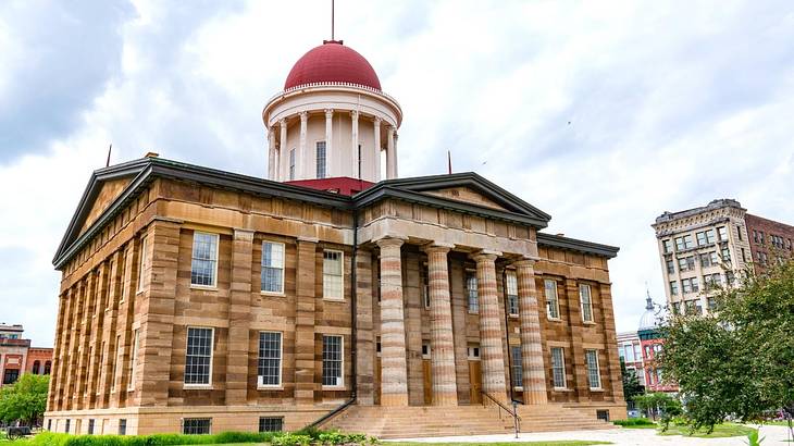 A neoclassical capitol building against a red dome, under a cloudy sky A neoclassical capitol building against a red dome, under a cloudy sky