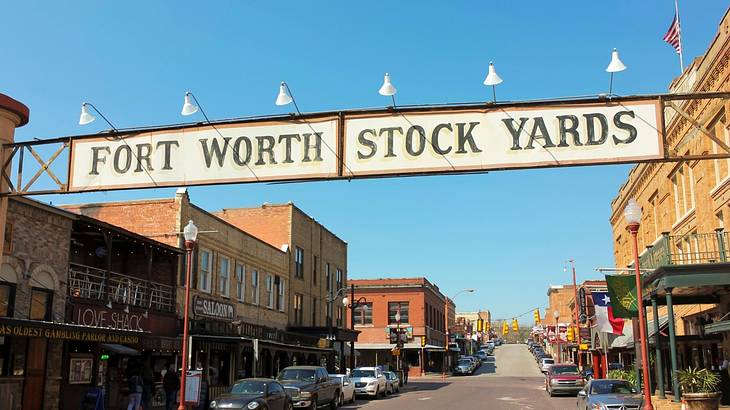 A sign that says "Fort Worth Stock Yards" over a street with old-fashioned buildings