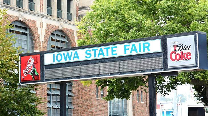 A big signboard of Iowa State Fair against a tree and a brick building