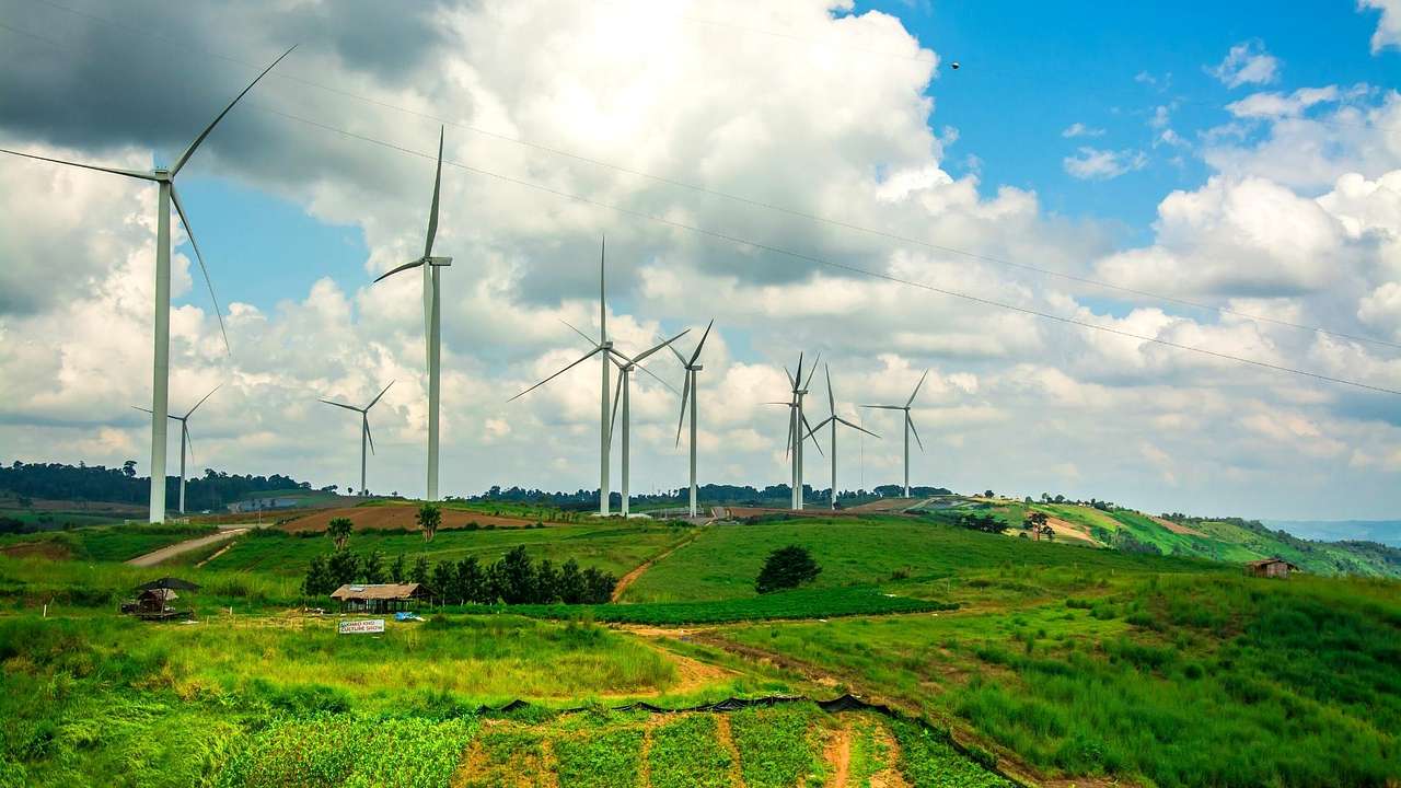Wind turbines lined up on an empty green field under a partly cloudy sky
