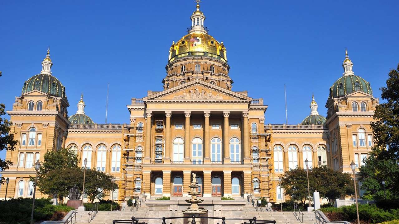 A neoclassical capitol building with one golden dome and four dark green domes