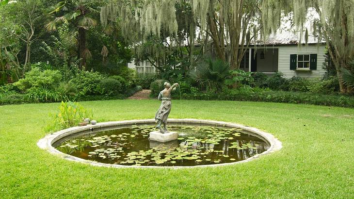 A pond with a small statue surrounded by grass and trees