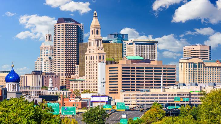 A skyline of modern downtown buildings with a road and trees in front A skyline of modern downtown buildings with a road and trees in front