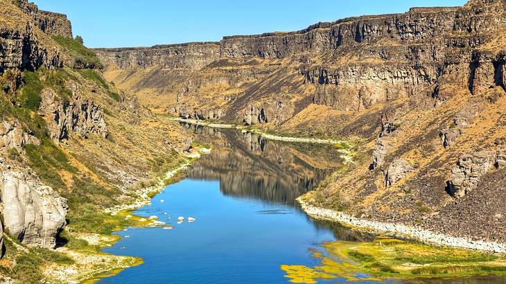 A blue reflective river meandering through a rugged canyon under a clear blue sky A blue reflective river meandering through a rugged canyon under a clear blue sky