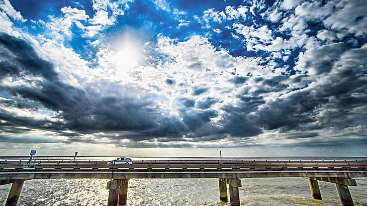 Looking at a concrete bridge with a car over water under a partly cloudy sky