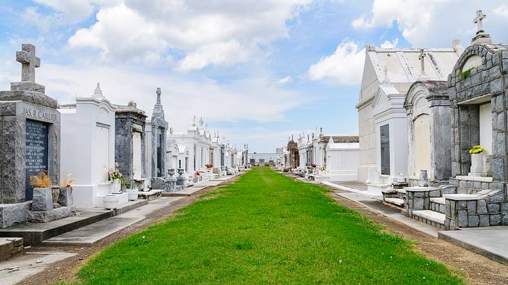 A pathway of green grass with white graves on each side under a partly cloudy sky A pathway of green grass with white graves on each side under a partly cloudy sky