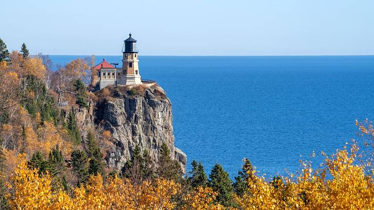Autumn trees against a lighthouse on the edge of a cliff overlooking blue waters