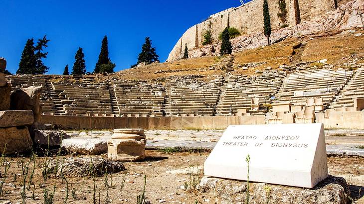 A white slab with the text "Theatre of Dionysus" against the ancient theatre seating
