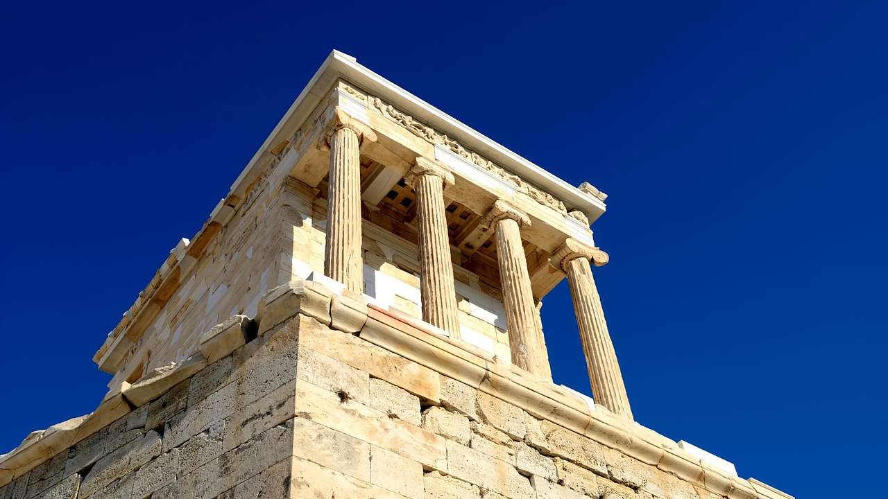 Looking up at an ancient marble structure with columns against a clear blue sky