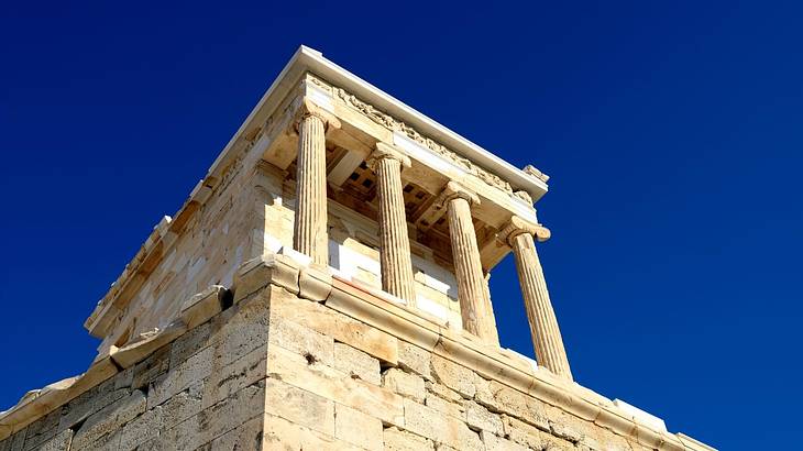 Looking up at an ancient marble structure with columns against a clear blue sky