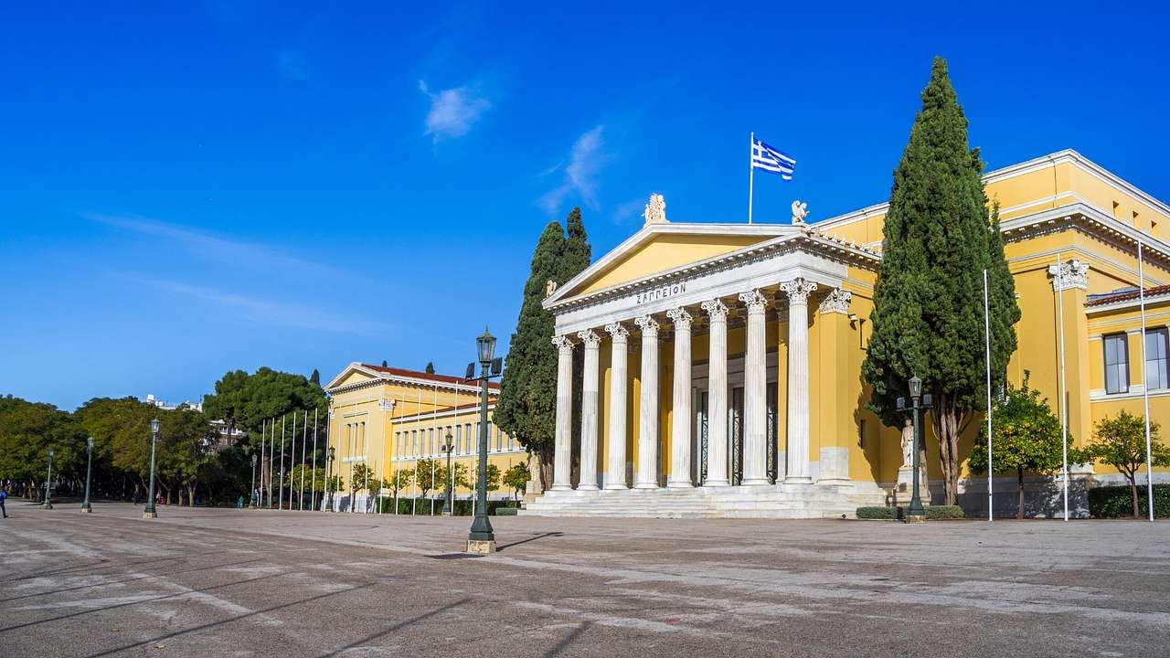 A neoclassical yellow building with white columns and trees outside, facing a road