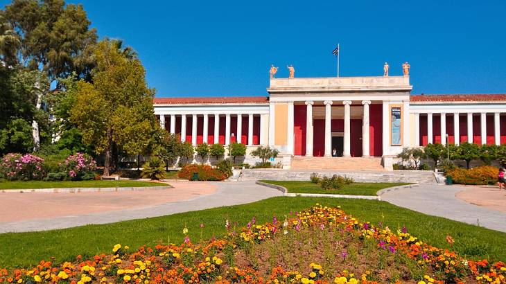 A red neoclassical building with white columns. facing a walkway with flowers