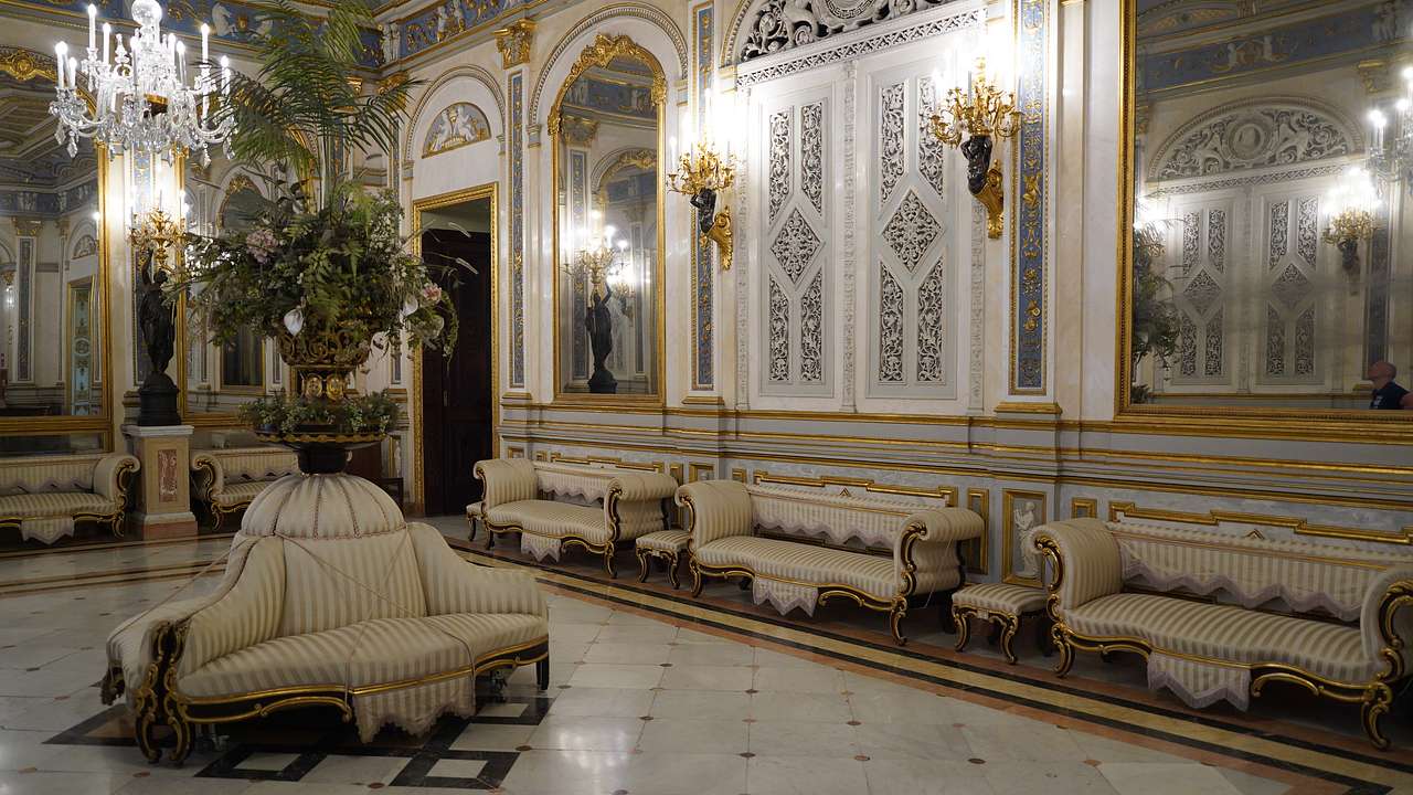 White-tiled floor with ornate art-covered walls with a white antique sofa