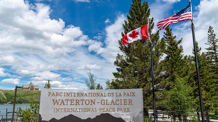Flags of Canada and USA at the right side of a park signage with trees in the back Flags of Canada and USA at the right side of a park signage with trees in the back
