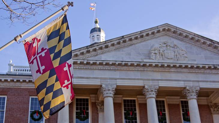 A red, yellow, and black Maryland state flag next to a columned building A red, yellow, and black Maryland state flag next to a columned building