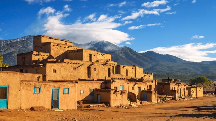 Ancient dwellings with blue doors against mountains under a partly cloudy sky
