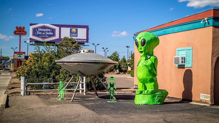 A life size green alien model and a gray UFO facing a road