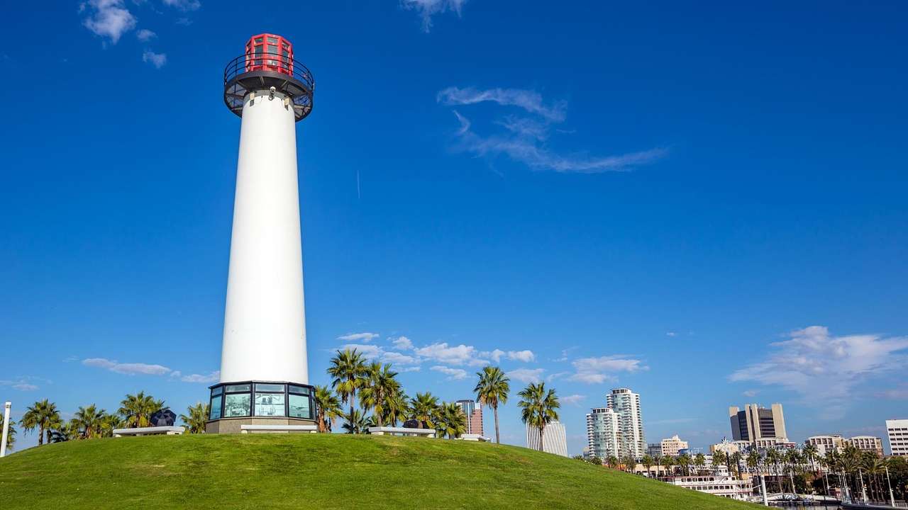 A white lighthouse with a red top sitting on a green hill under a blue sky