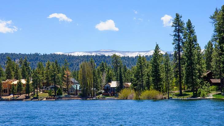 A lake next to cabins and trees with a snow-capped mountain range in the distance