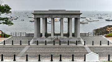 A gray neoclassical monument with columns against the water with white boats