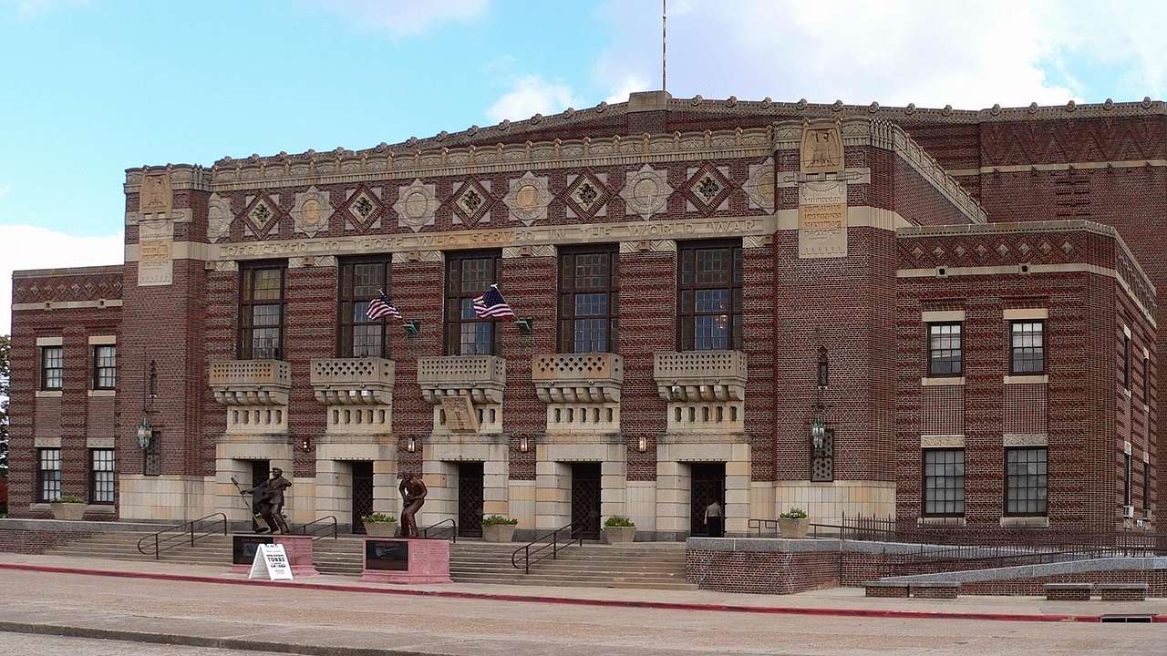 A red brick building with a stone pattern and statues and flags in front of it
