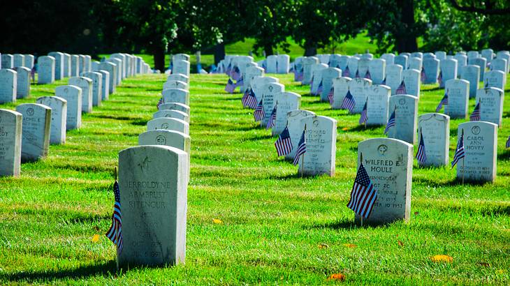 US flags in front of marble tombstones arranged in a grid on a grassy graveyard