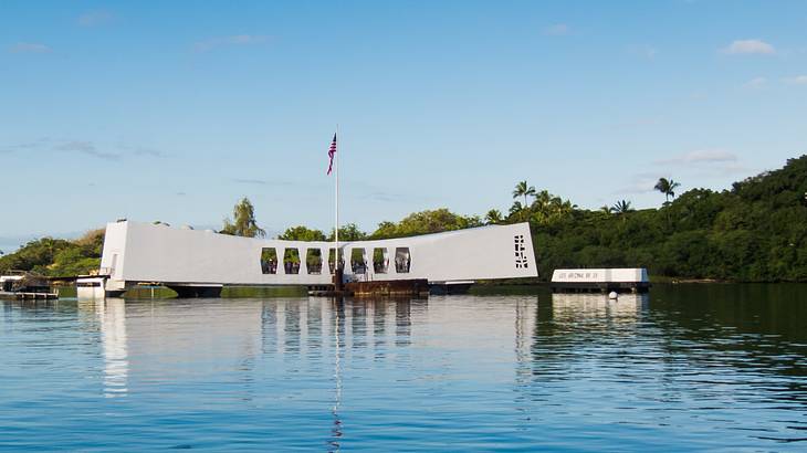 An American flag atop a white structure set above the water of a harbor