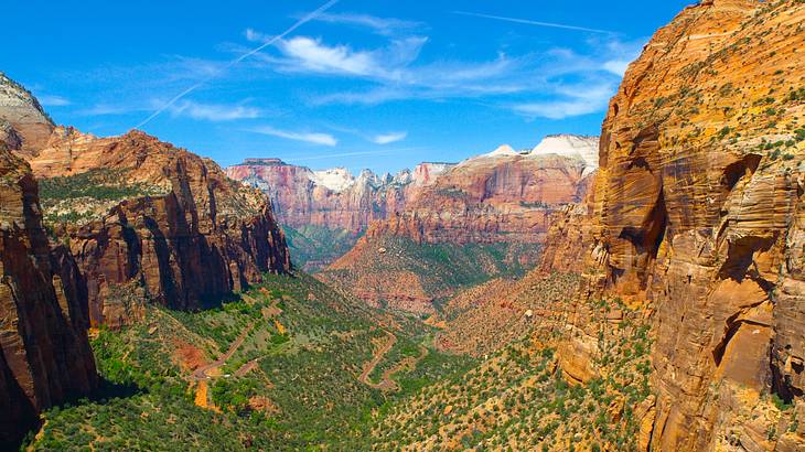 A green valley below the red cliffs of layered rock formations