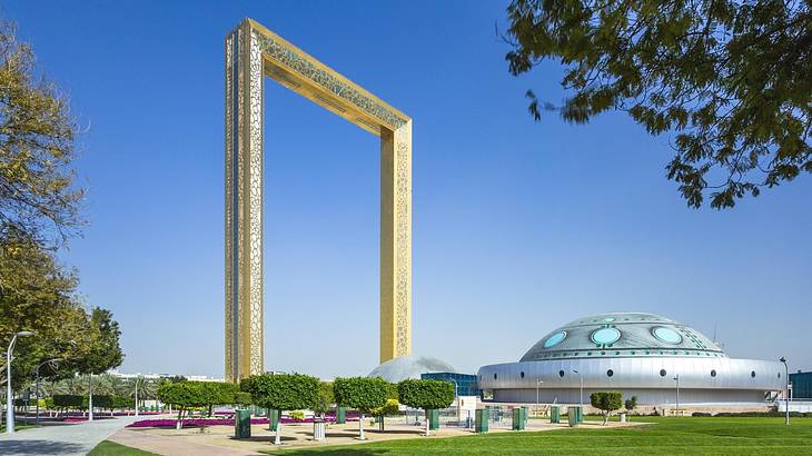 A large gold frame structure in a park next to a space-ship-like structure