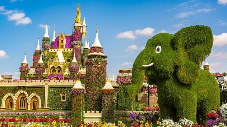 A princess castle covered in flowers and greenery next to a topiary elephant