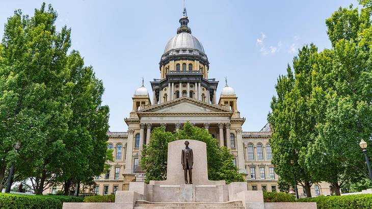 A large stone building with a domed roof next to trees and an Abraham Lincoln statue