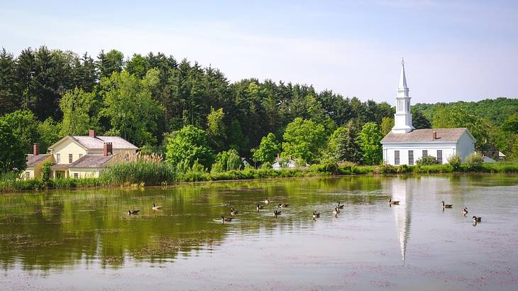 A lake next to lots of green trees, a house, and a small white church