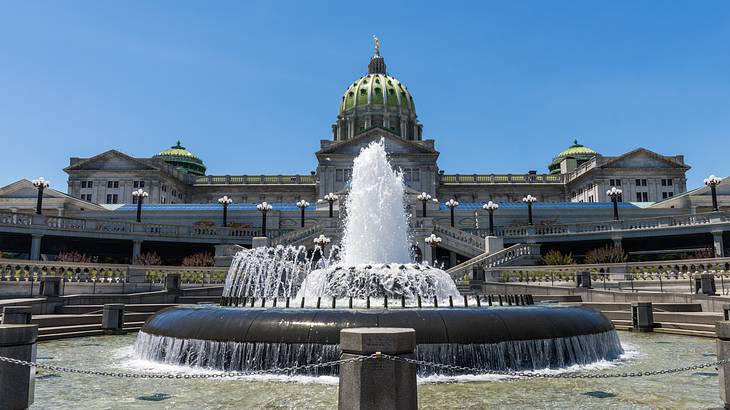 A water fountain in front of a building with a dome on a clear day