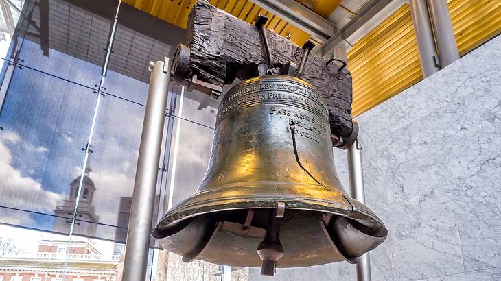 An old bell made of bronze and copper with a crack in it hanging on display
