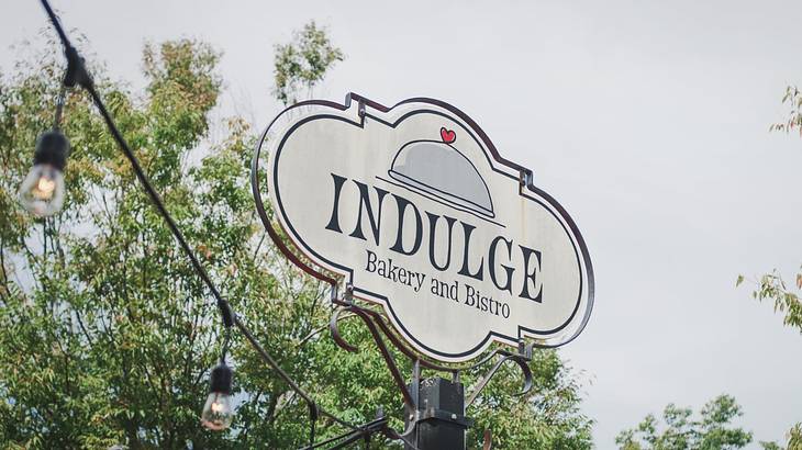 A sign that says "Indulge Bakery and Bistro" next to string lights and trees