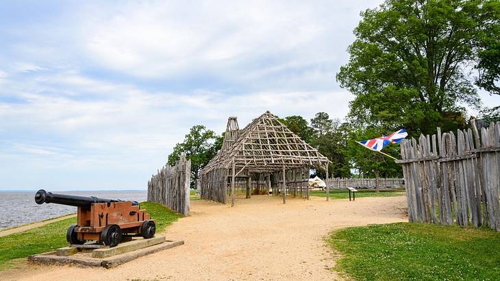 A canon and old structure next to a sand path and grass, with the ocean to the side A canon and old structure next to a sand path and grass, with the ocean to the side