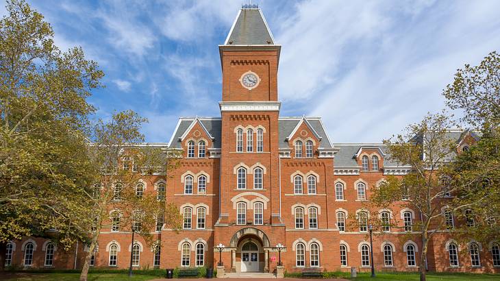 The exterior of a brown building with a clock tower and trees in front The exterior of a brown building with a clock tower and trees in front
