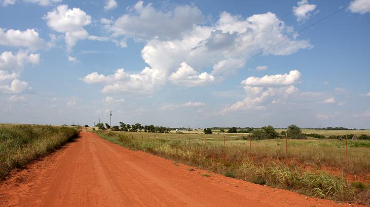 A road made of reddish soil with grassy fields on either side