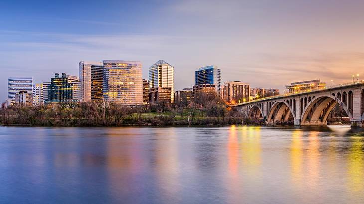 A river with a bridge over it next to city buildings at dusk A river with a bridge over it next to city buildings at dusk