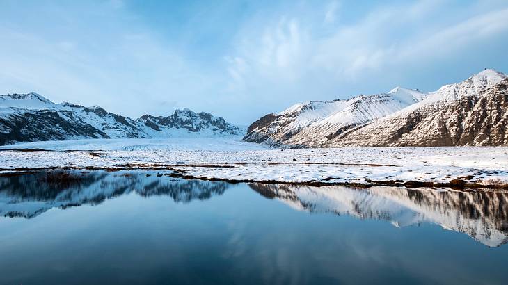 A lake surrounded by snow-covered mountains under an icy blue sky