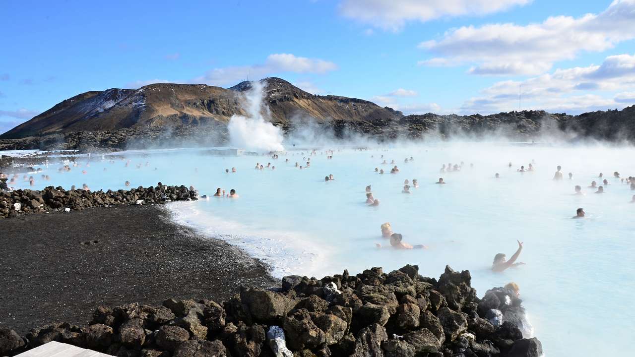 People batheing in a steaming blue pool surrounded by rocks and hills