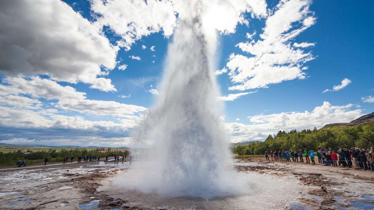 A famous Iceland landmark-a geyser spraying water with trees and tourists to the side