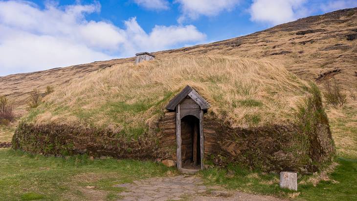 A small grass-covered hill with a door in the middle under a blue sky with clouds