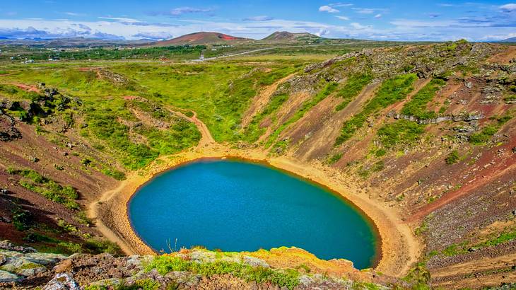 An emerald lagoon in a grass-covered crater with hills in the distance