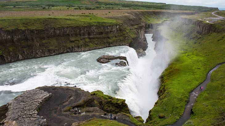 An aerial view of a waterfall with white spray surrounded by grassy hills