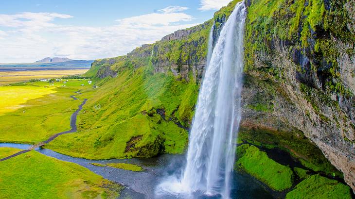 A waterfall flowing into a small pool with green grass and hills around it