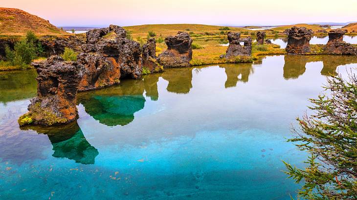 An emerald lake with rock formations in it next to grassy hills