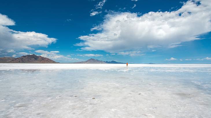 Vast salt flats with a person standing on them in the distance next to mountains Vast salt flats with a person standing on them in the distance next to mountains